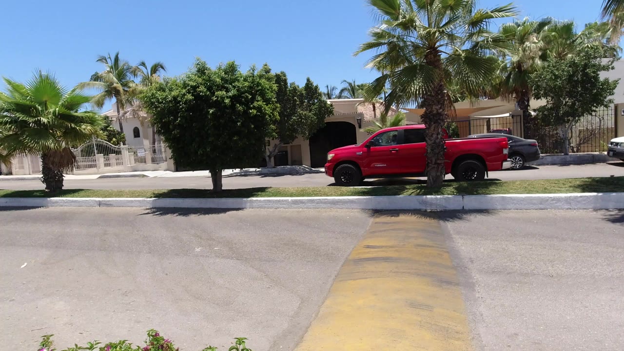 Red pickup truck on a sunny residential street with palm trees and gated homes.