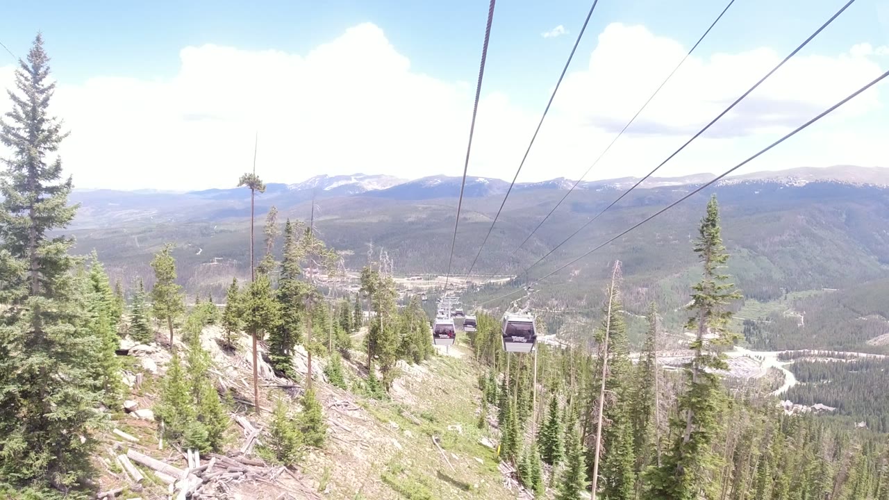 Gondola cables over evergreen mountain slope and distant ridges.