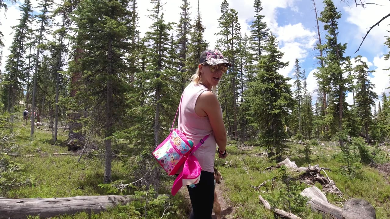 One second in, the woman is closer to the center of the Winter Park, Colorado forest path, with the dog partly visible near her legs and conifers filling the background.