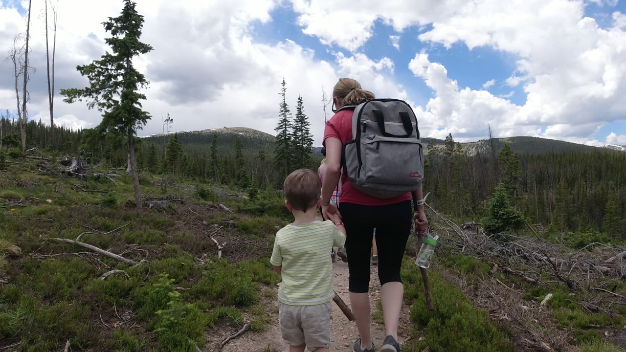Boy and woman hiking on a mountain trail under large clouds.