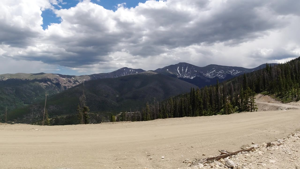 Mountain panorama with forested hills, snow patches, and cloudy sky.
