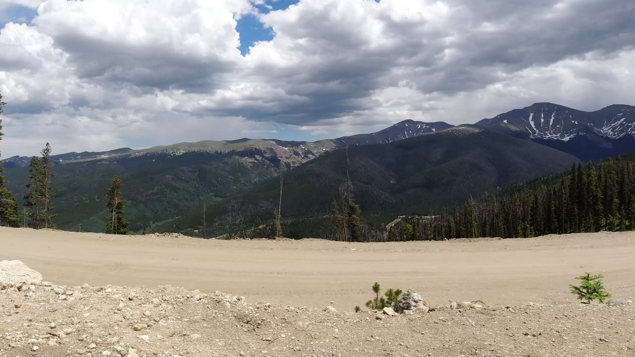 Dirt road overlook with forested mountains and cloudy sky.