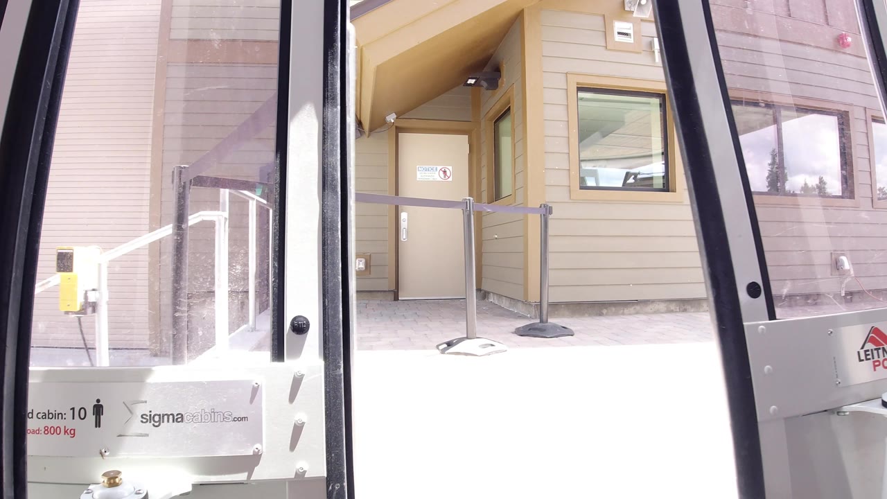 At 0:01 in Winter Park, Colorado, the vehicle door remains in the foreground with a beige wall, small exterior window, entrance area, and no visible people behind the glass.