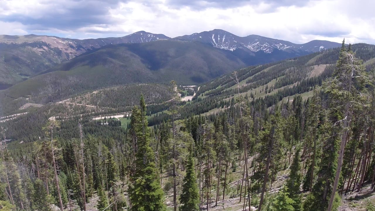 Wide view from Winter Park, Colorado over evergreen forest toward layered mountain ridges and patchy snow, with no visible people.