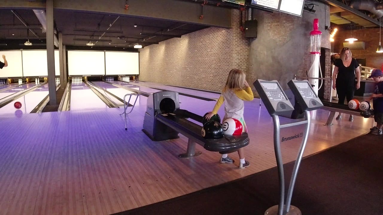 Young girl beside a bowling ball return in a bowling alley.