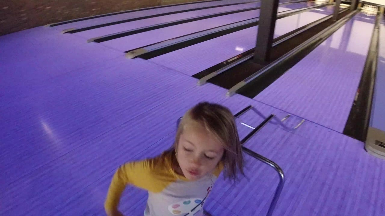 Young blonde girl near purple-lit bowling lanes.