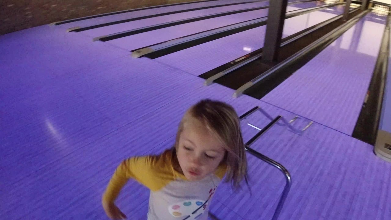 The blonde girl looks downward near the lane edge as purple light reflects across the bowling surface in Winter Park, Colorado.