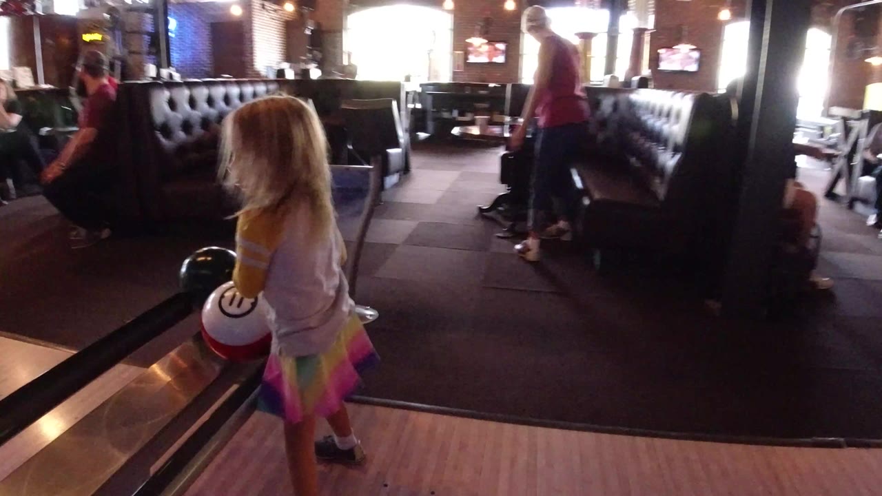 Blond child beside a bowling lane holding a white bowling ball.