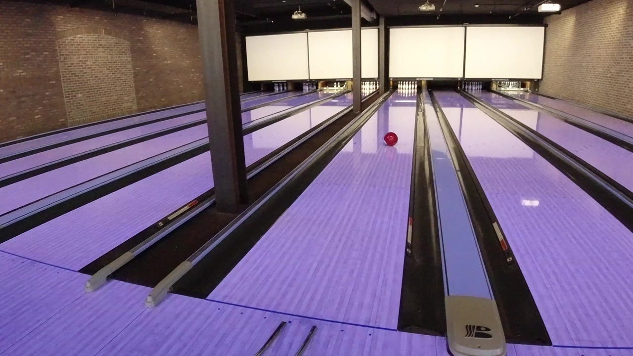 Red bowling ball rolling on a purple-lit lane inside a bowling alley.