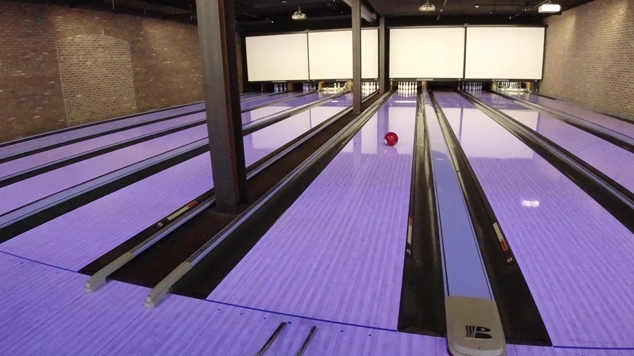 At 0:01, the red ball has moved farther toward the pins on the purple-lit lane in Winter Park, Colorado, with dark gutters and brick side walls visible and no visible people.