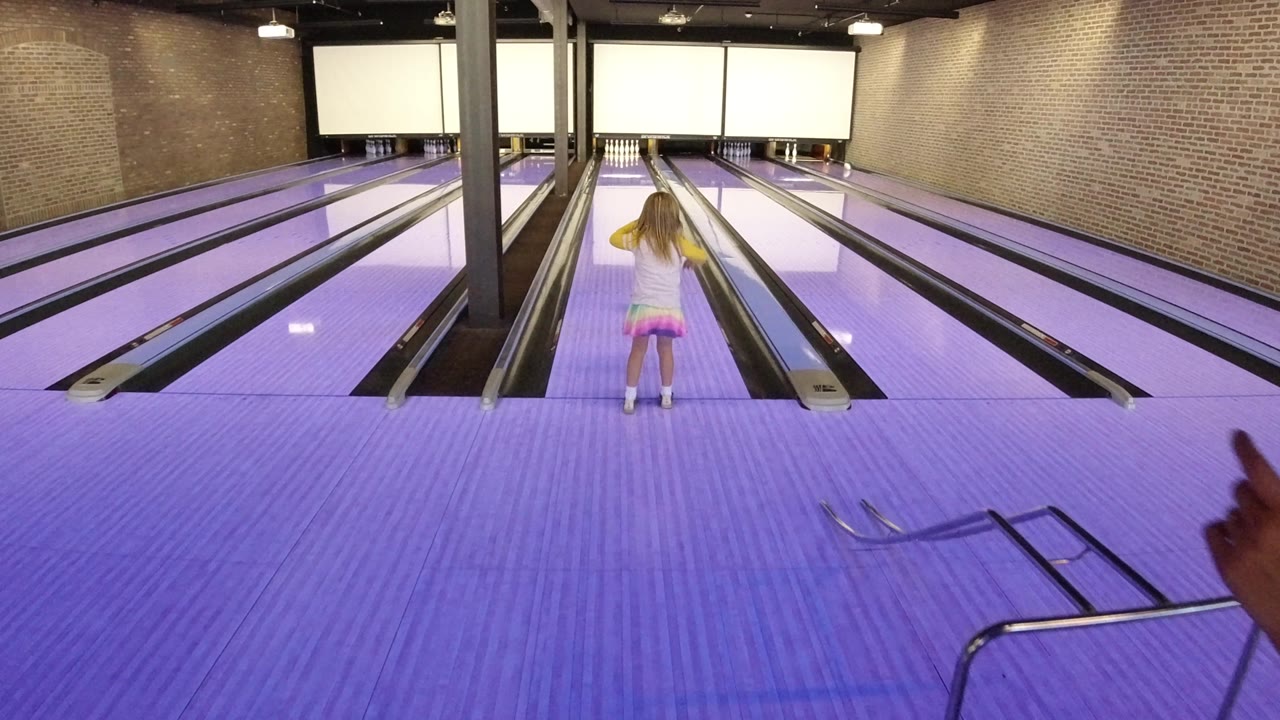 The child stands centered between bowling lanes in Winter Park, Colorado as the thrown ball moves away toward the pins under bright lane lighting.