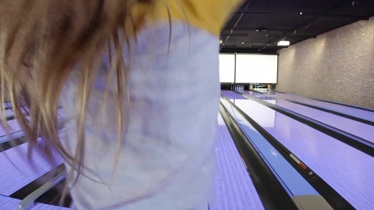 Child close to the camera beside purple-lit bowling lanes.