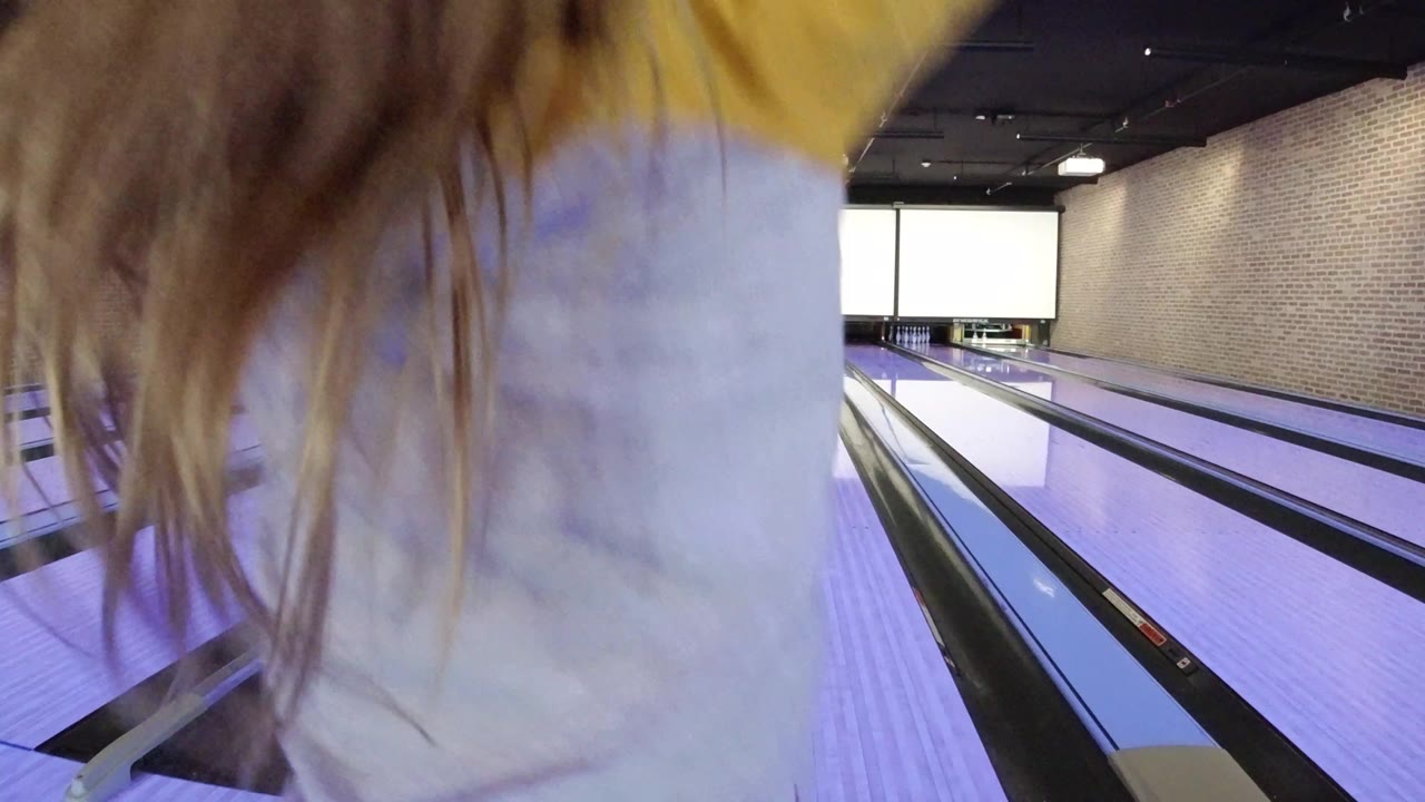 The child remains close in the foreground while the purple-lit bowling lanes and brick wall stretch toward the pins in Winter Park, Colorado.