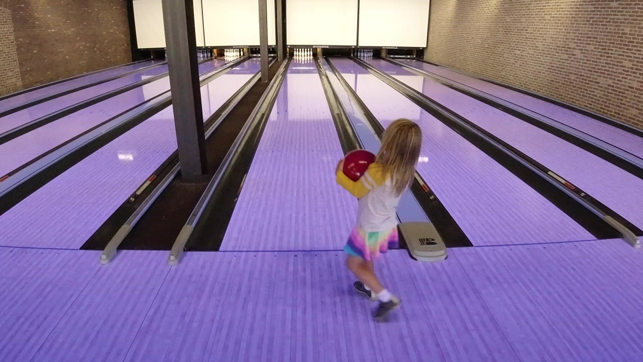 Young girl holding a red bowling ball at the lane approach.