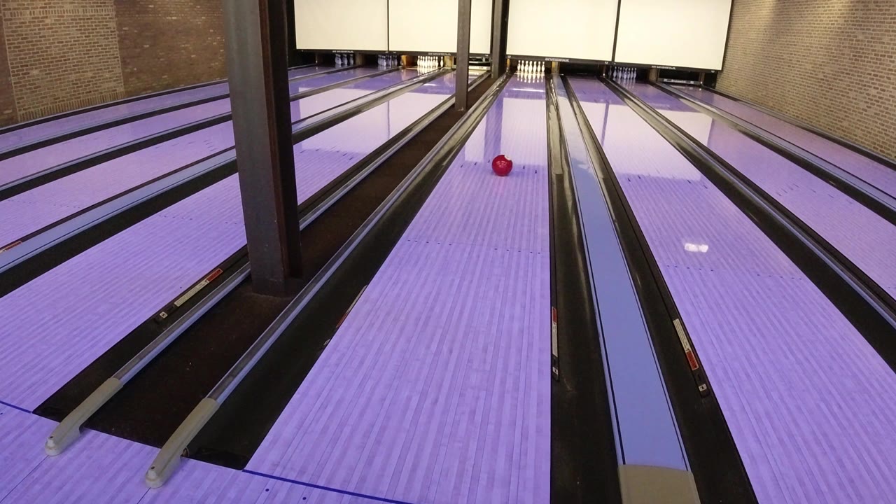 The red ball continues down the center area of the purple-lit lane in Winter Park, Colorado, with gutters and brick walls framing the view and no visible people.