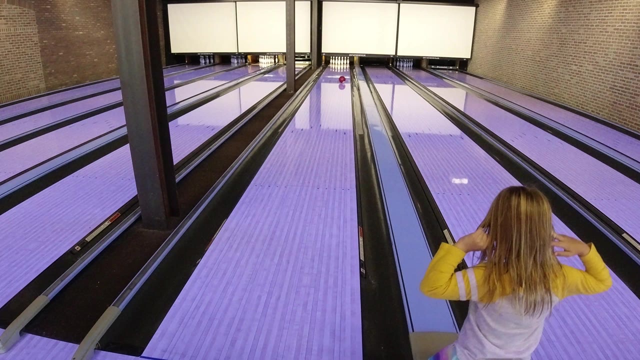 Girl facing purple-lit bowling lanes from behind.