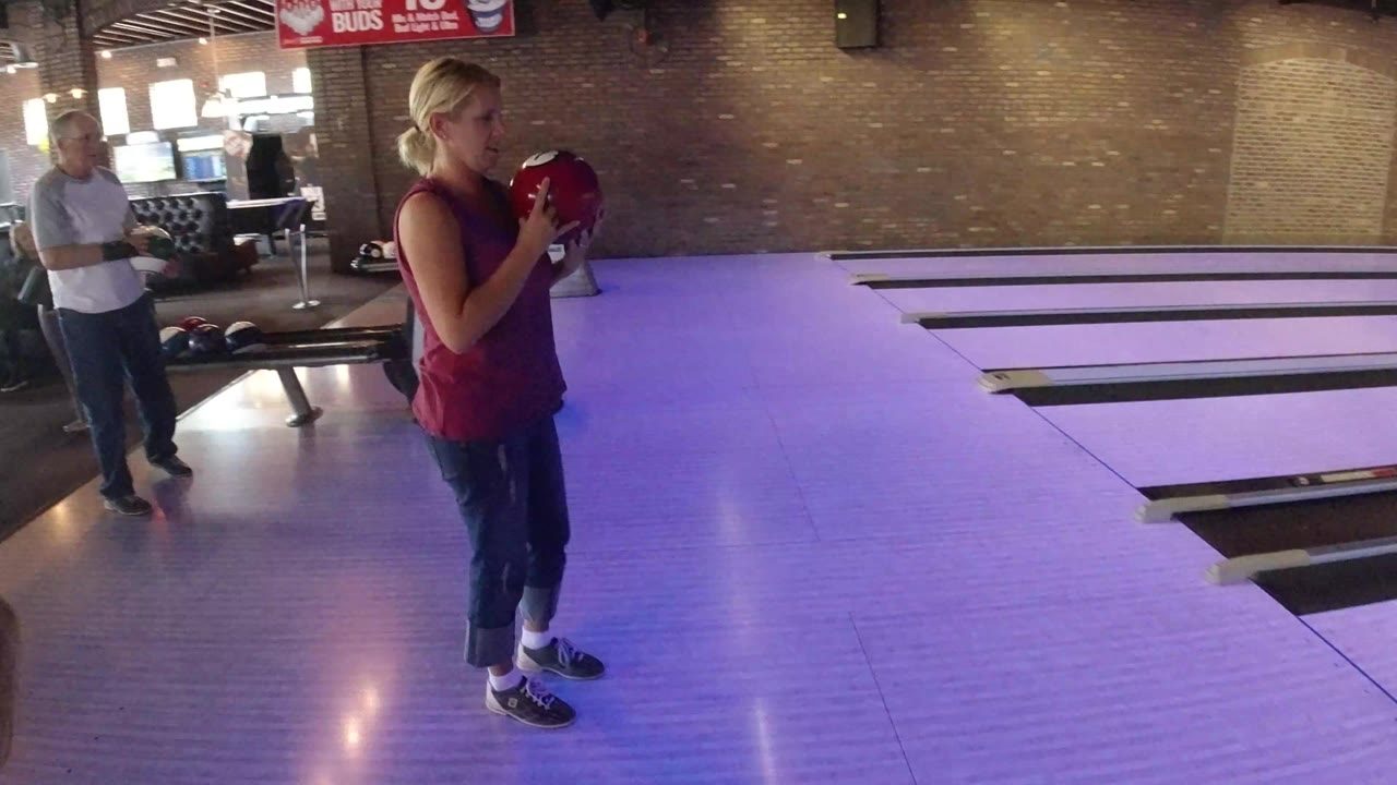In Winter Park, Colorado, a blonde woman stands at a bowling lane holding a red ball, with an adult man, brick walls, seating, and beer signage behind her.