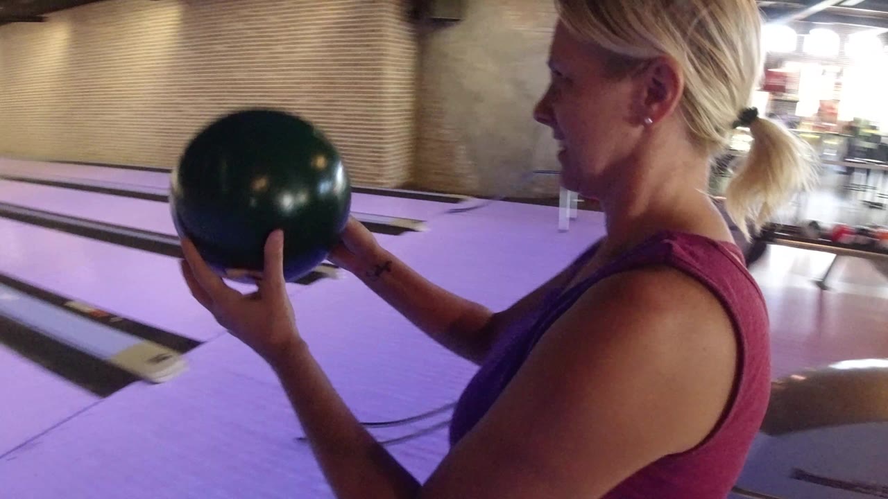 Woman holding a bowling ball beside a purple-lit lane.