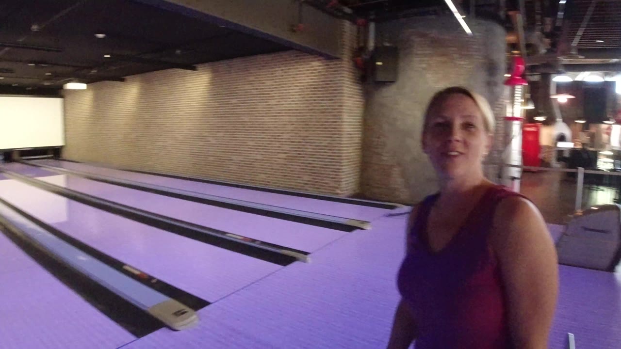 Woman standing beside purple-lit bowling lanes.