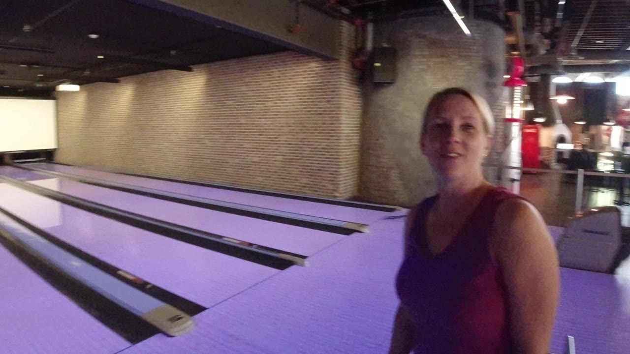 Purple-lit bowling lanes run into the background while the woman is partly cropped at the right edge inside the Winter Park, Colorado bowling alley.