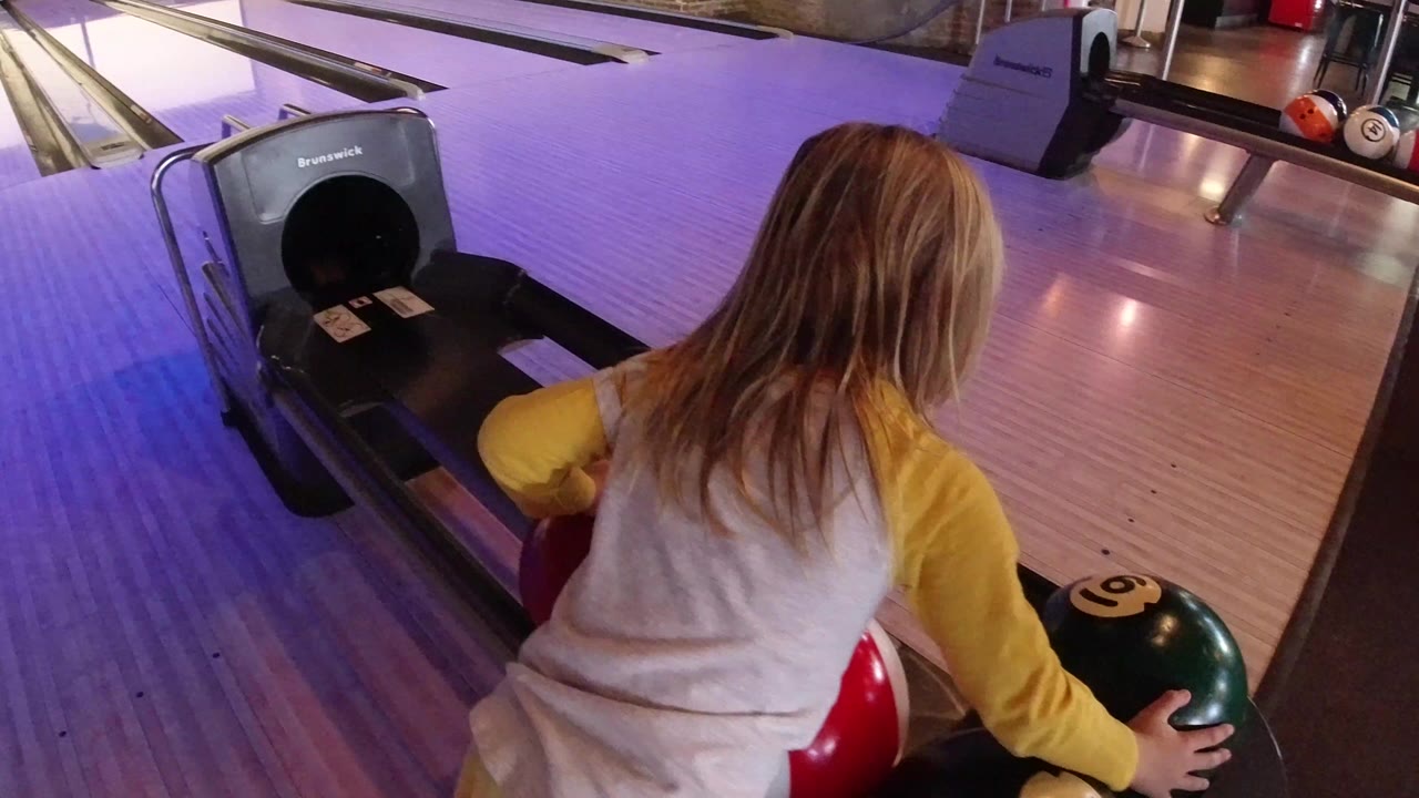 Young girl reaches toward bowling balls at a lane return.