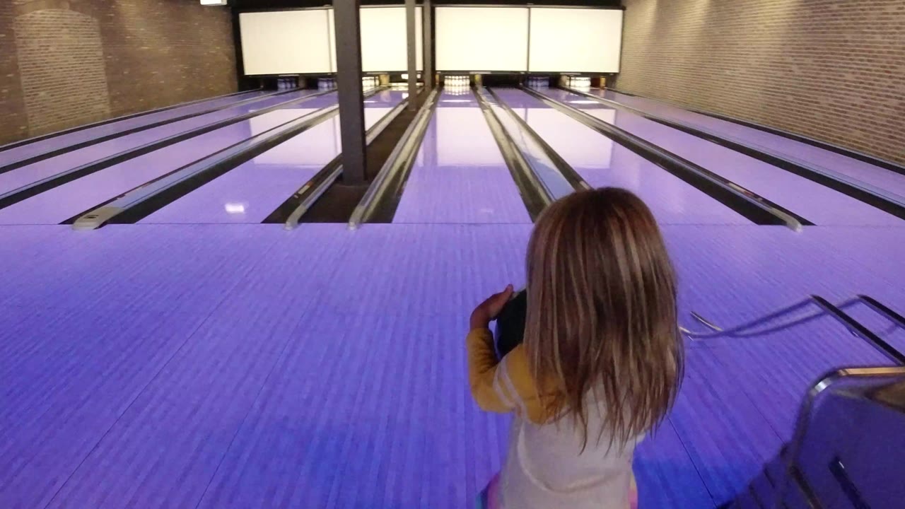 Child seen from behind at a purple-lit bowling lane.