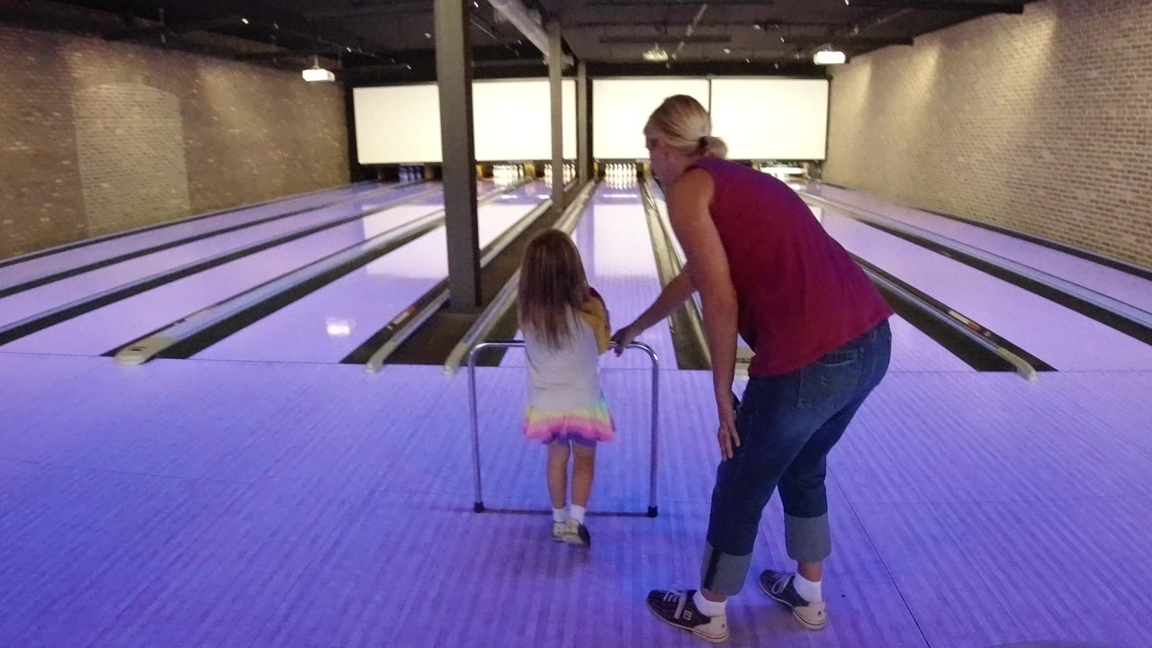 Adult helps a child line up at a bowling ramp.