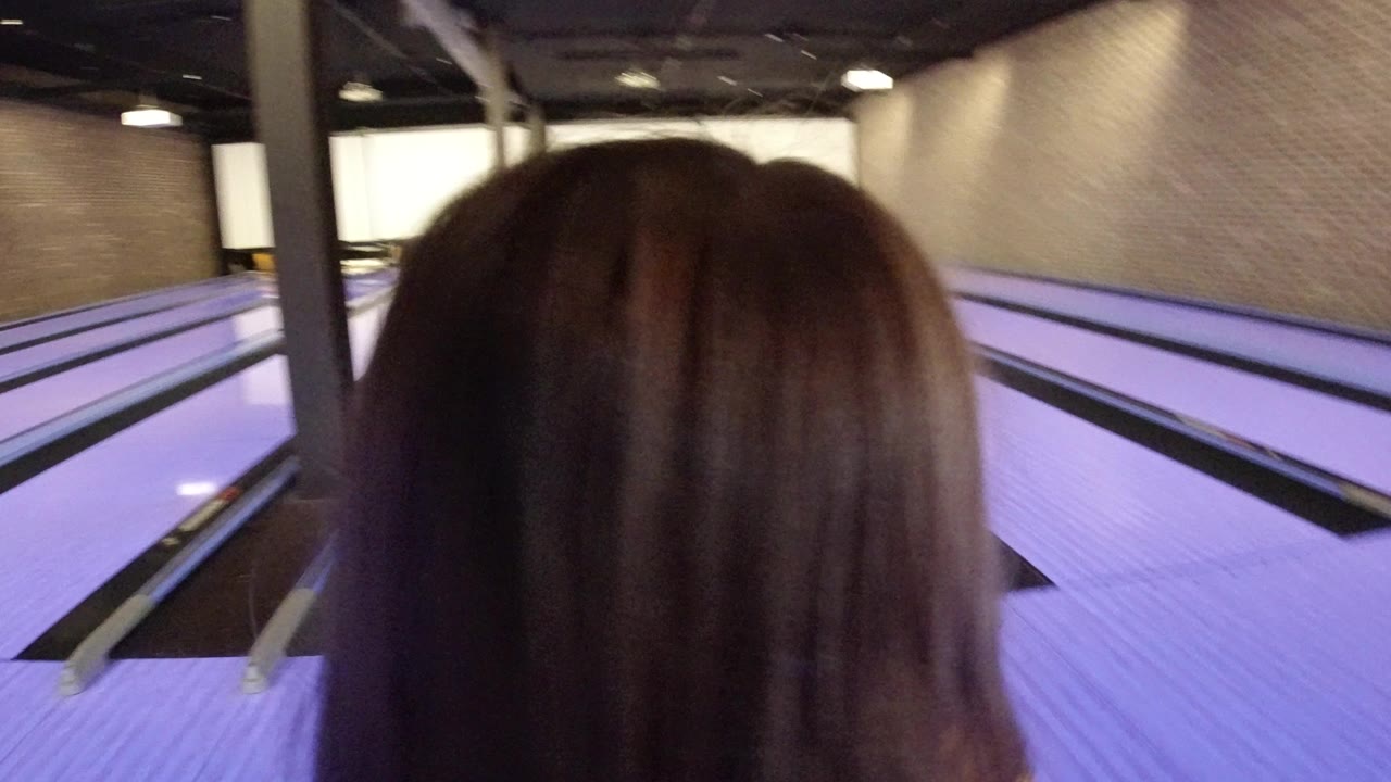 A child seen from behind faces purple-lit bowling lanes in Winter Park, Colorado, with brick walls and overhead fixtures beyond the lanes.