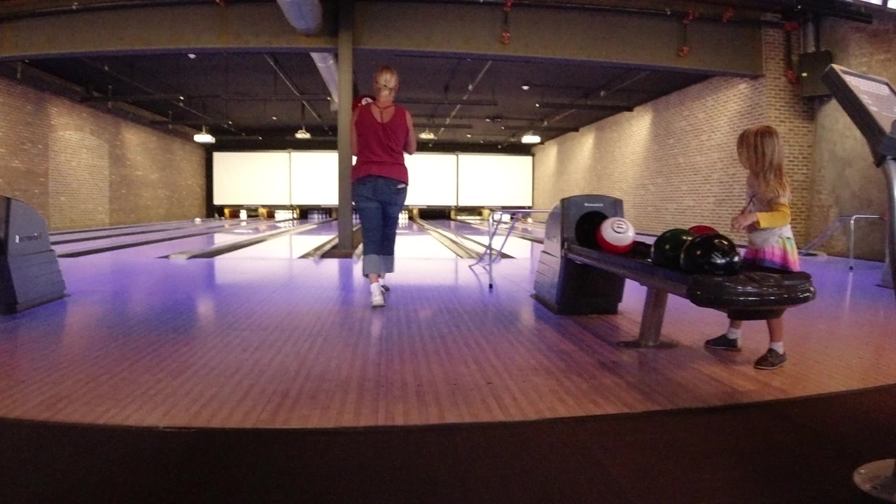 Woman and young girl at a bowling lane with balls on a return.