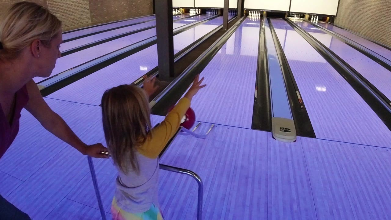 Woman helps a young girl at the start of a bowling lane.