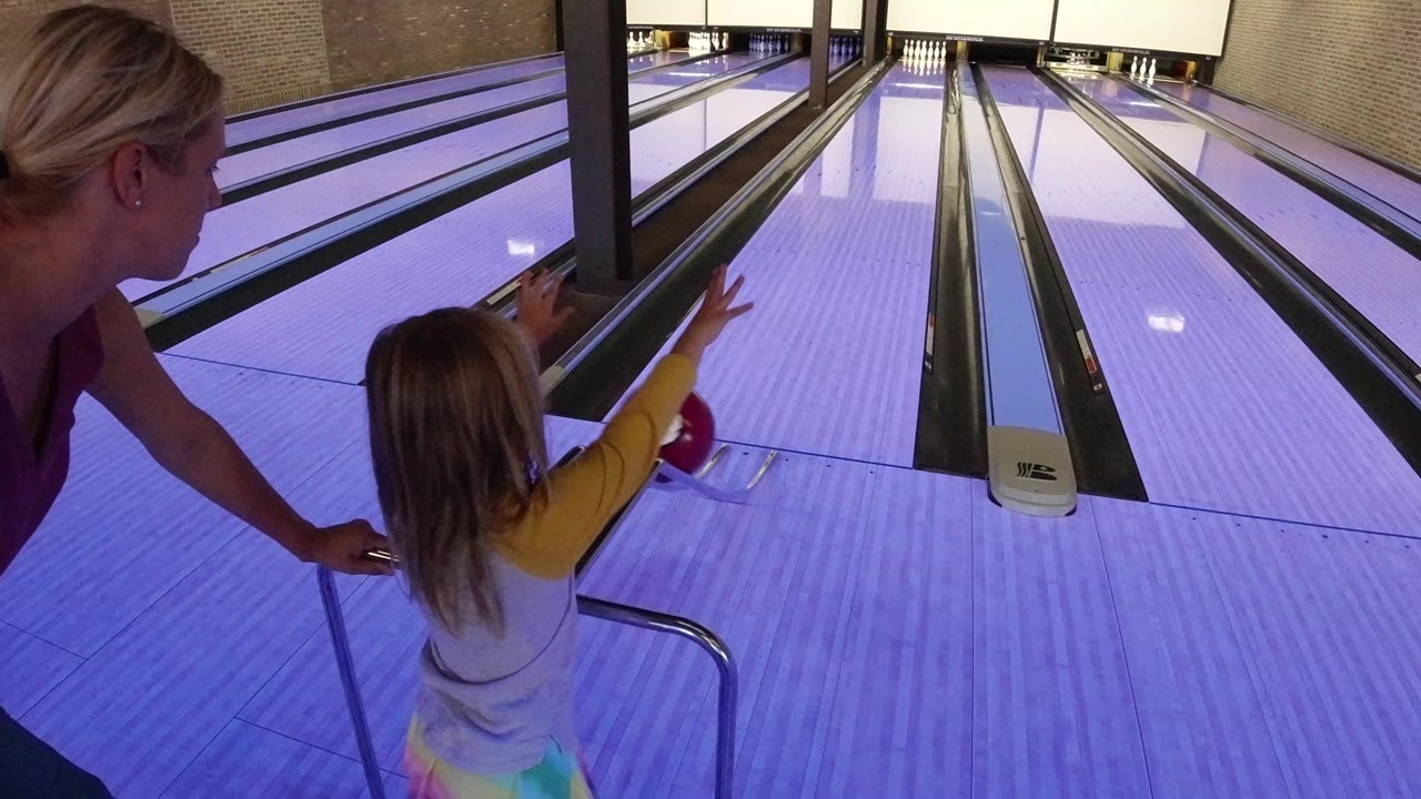 The young girl extends her arm toward the lane with the red bowling ball while the woman stays close at the left edge of the bowling approach in Winter Park, Colorado.