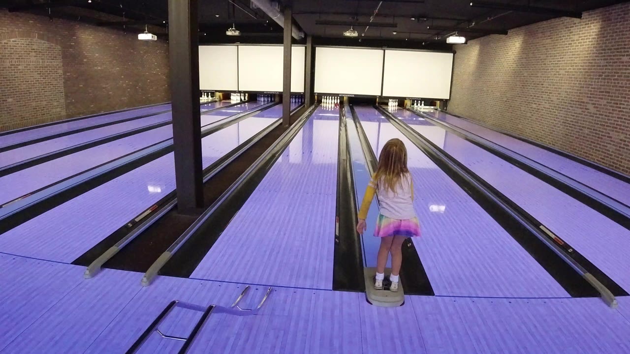 Young girl standing at the start of a bowling lane.