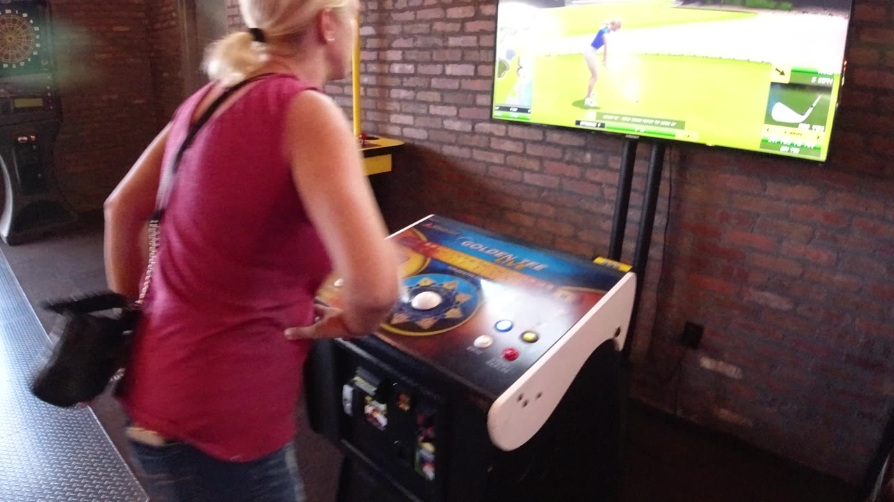 Woman approaches an arcade golf cabinet facing a wall-mounted TV.
