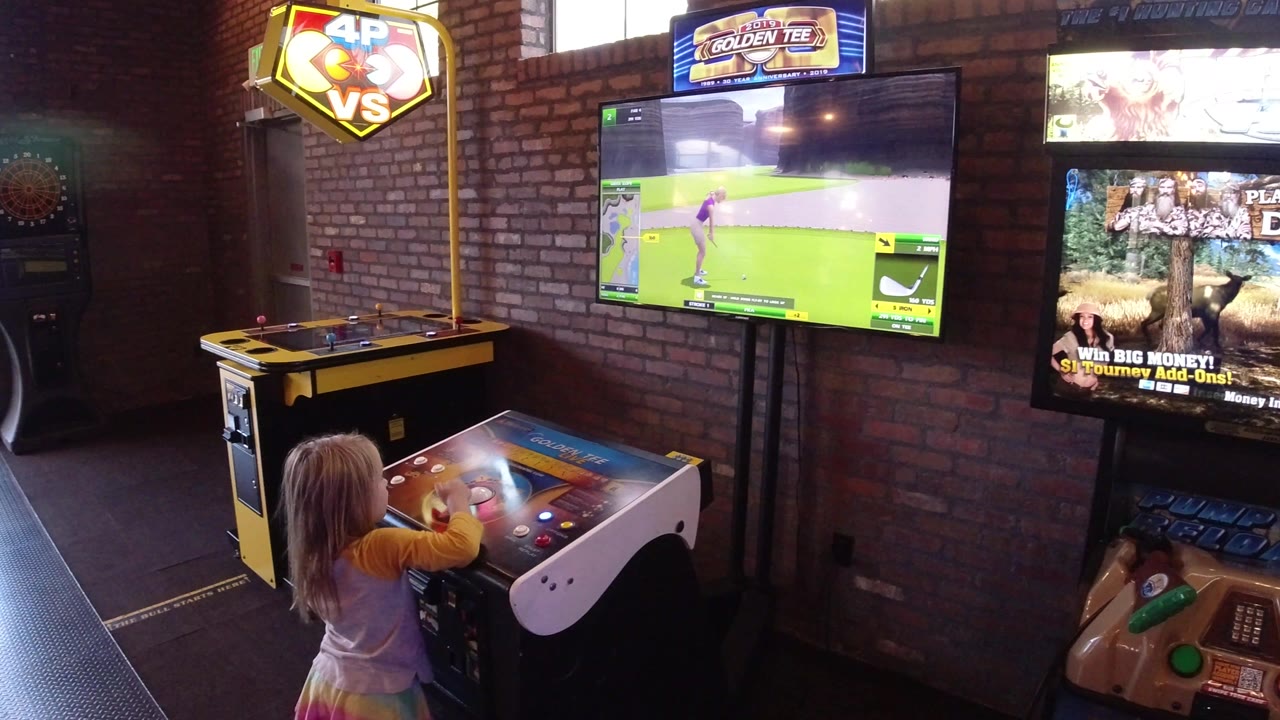Young girl at an arcade game console facing two glowing screens.