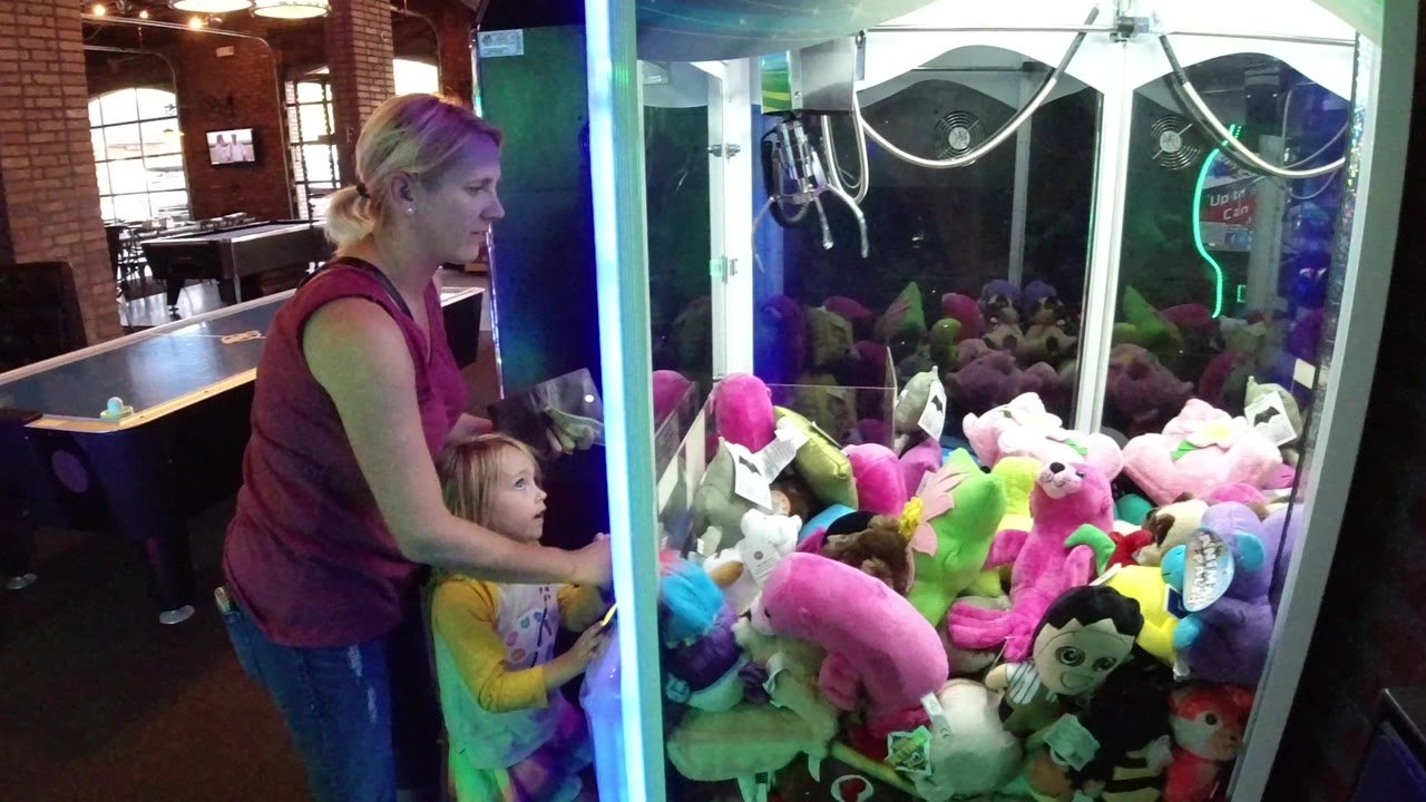 The mother leans close to the child as both look into the claw machine, with bright plush animals pressed against the front glass in Winter Park, Colorado.