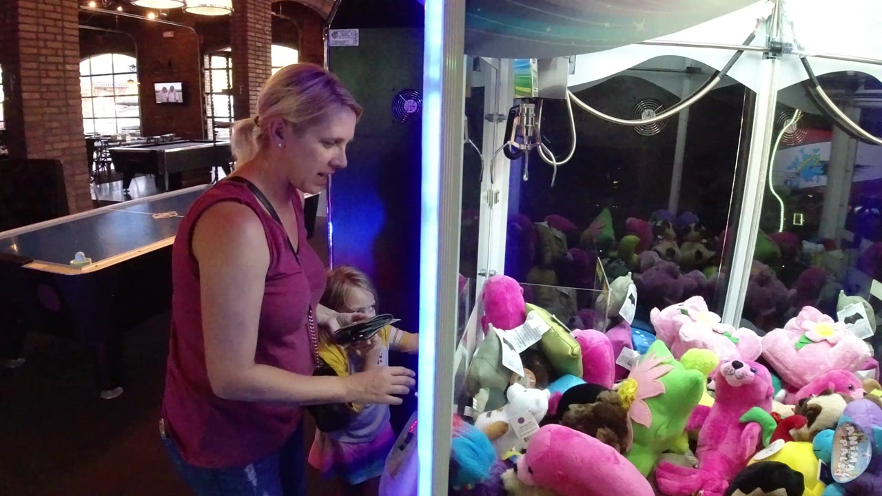 Woman and child beside a claw machine filled with plush toys.