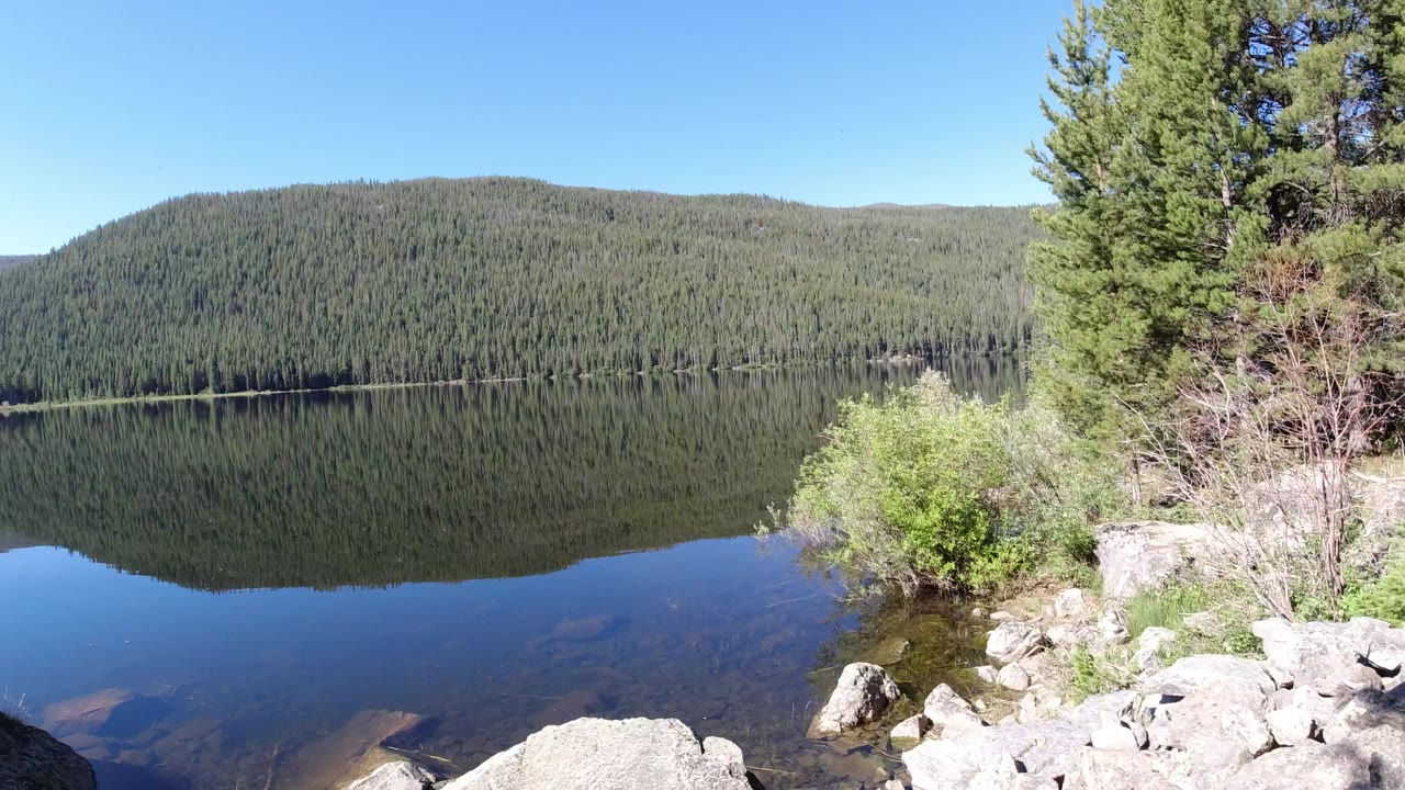 Mountain lake reflecting a forested hillside under blue sky.
