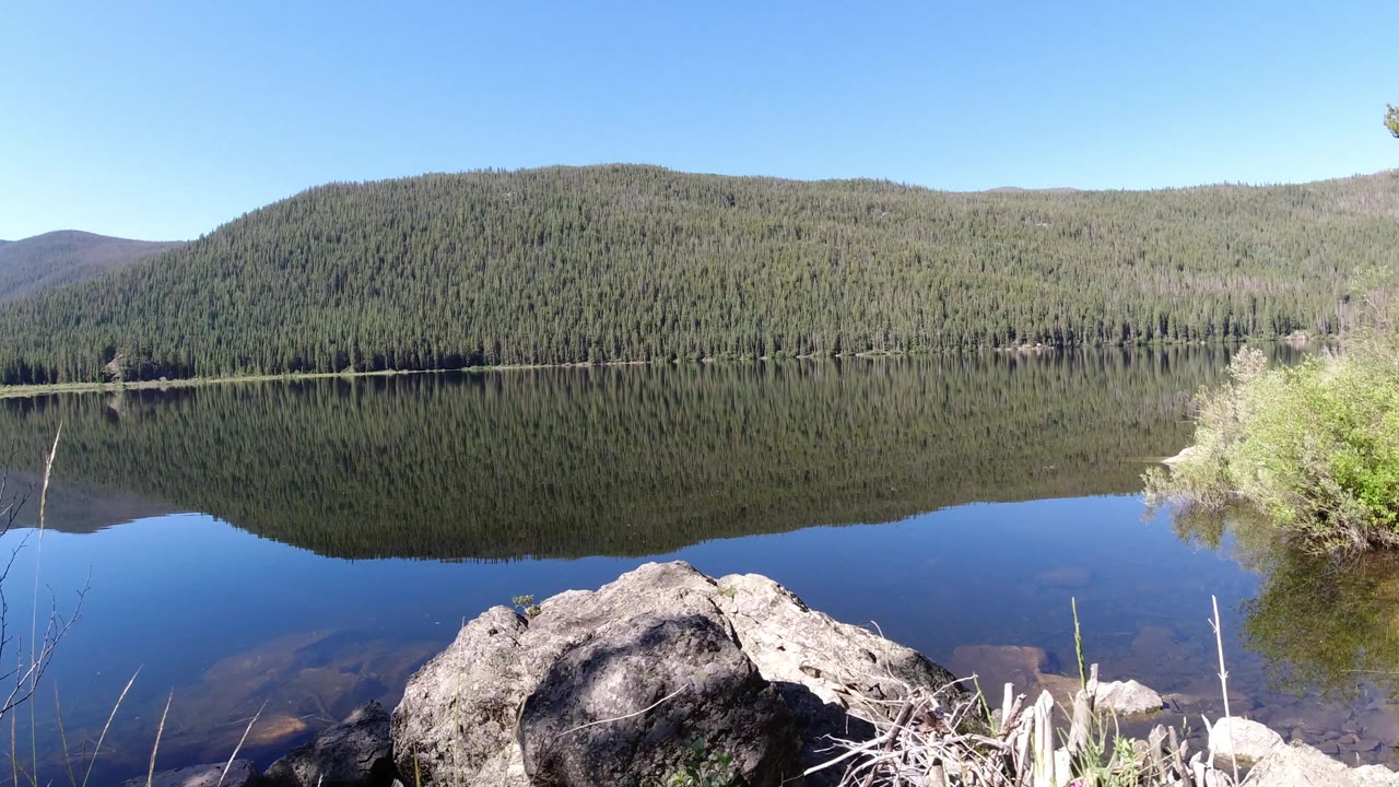 Large rock in the foreground with lake and forest reflection beyond
