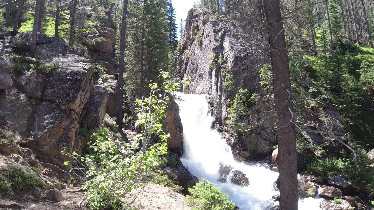 Waterfall dropping between rocks and tall trees beside a dirt path