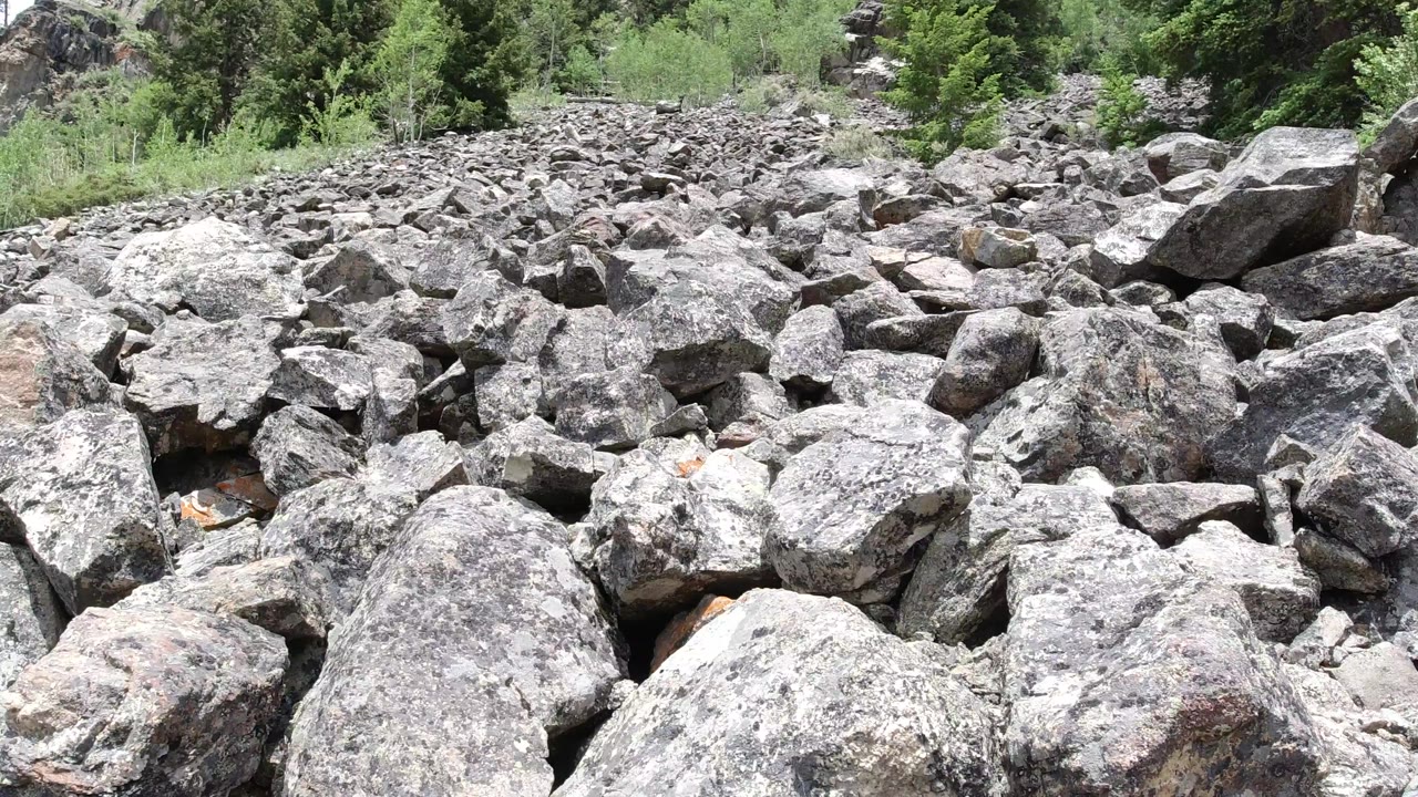 Winter Park, Colorado rocks fill the frame from foreground to horizon line, with scrubby green plants and conifers visible along the upper slope, and no visible people.
