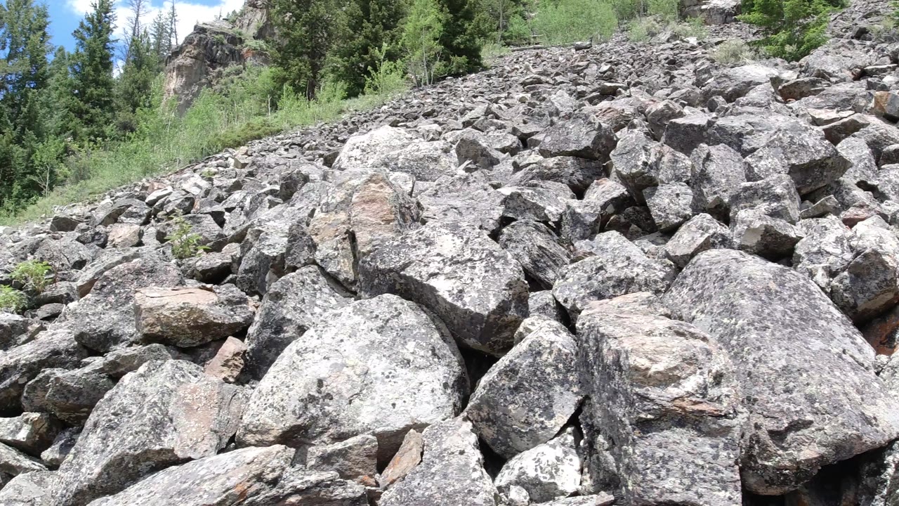 Boulder pile with trees and a small patch of blue sky behind it.