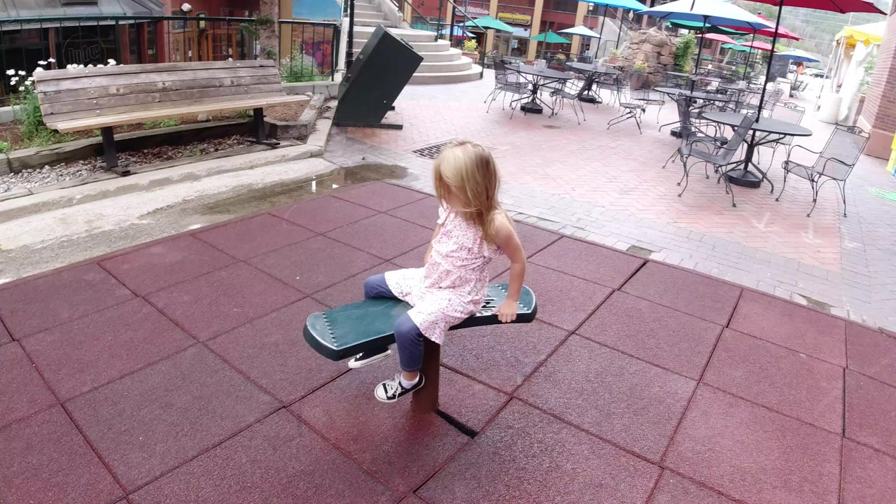 Young girl sitting on a green bouncy seat in an outdoor play area.