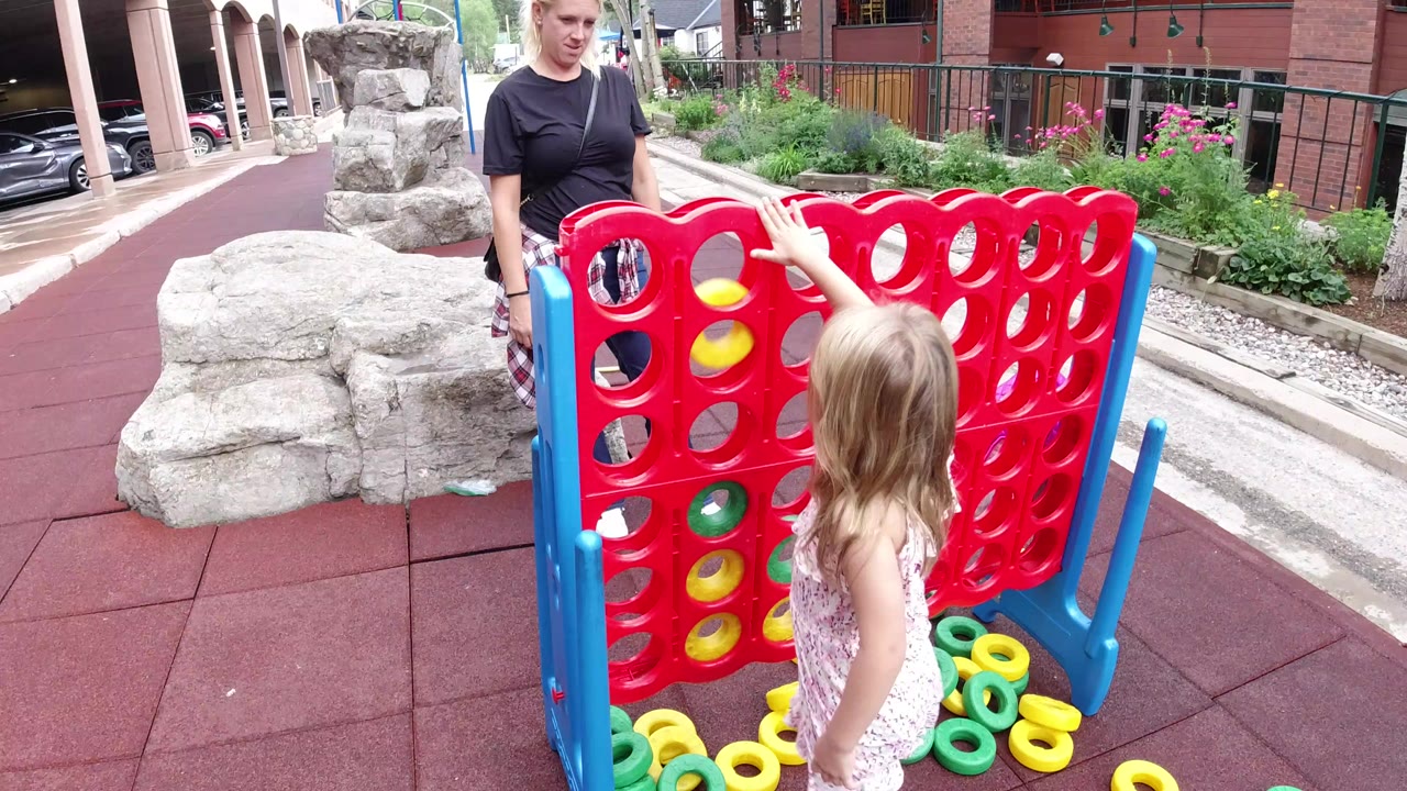 Child and adult beside a giant red Connect Four game outdoors.