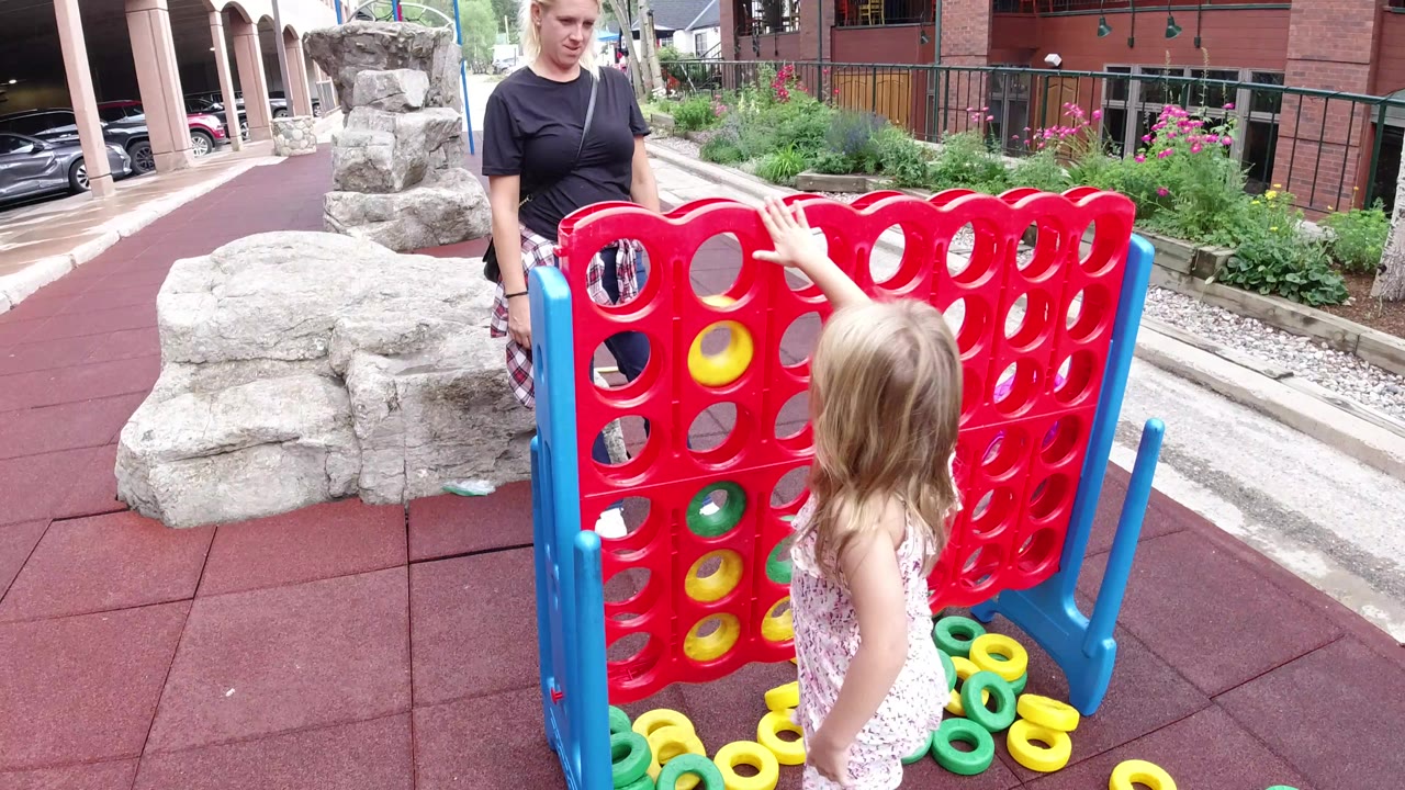 The child stands close to the red game grid as yellow and green rings sit in several slots and on the ground in Winter Park, Colorado.