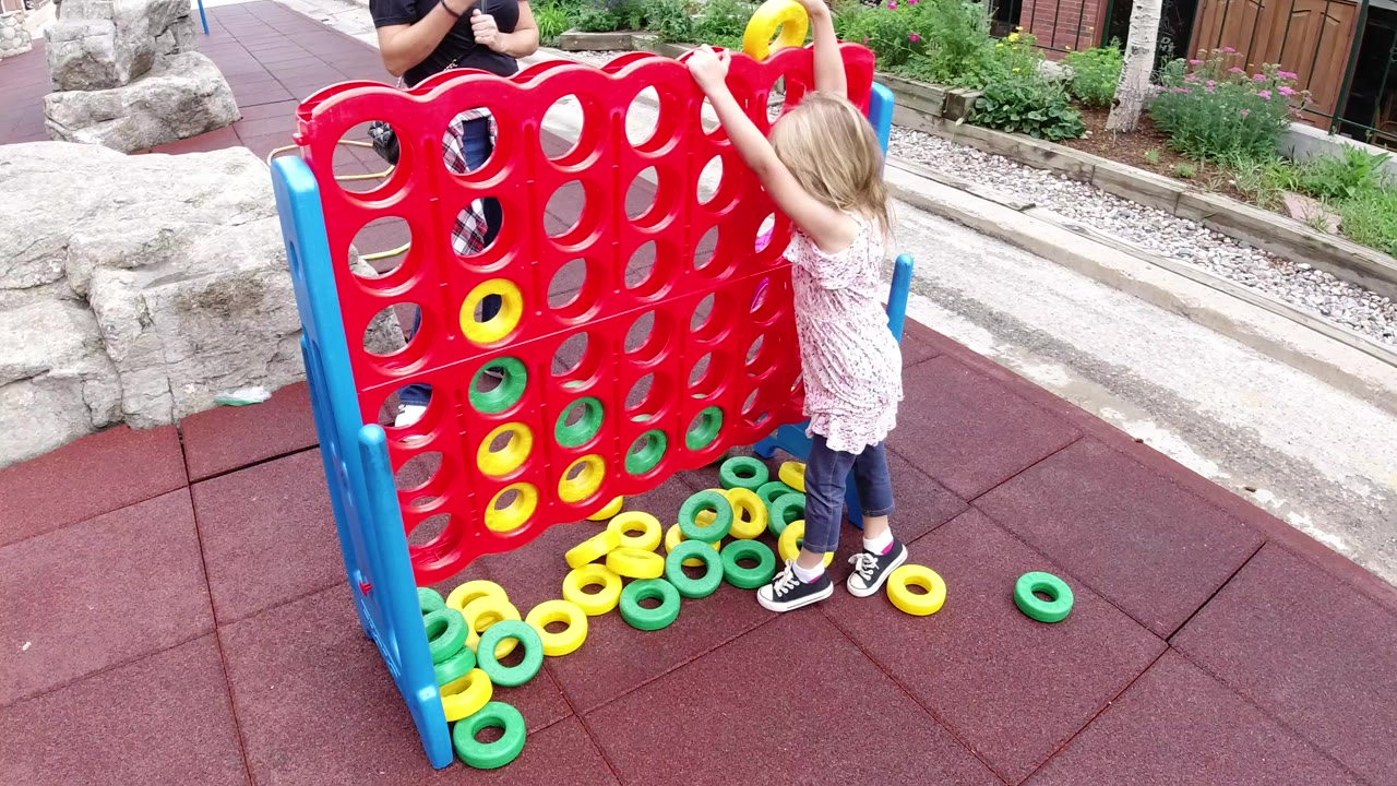 Young girl placing a yellow ring in a giant red outdoor game board.