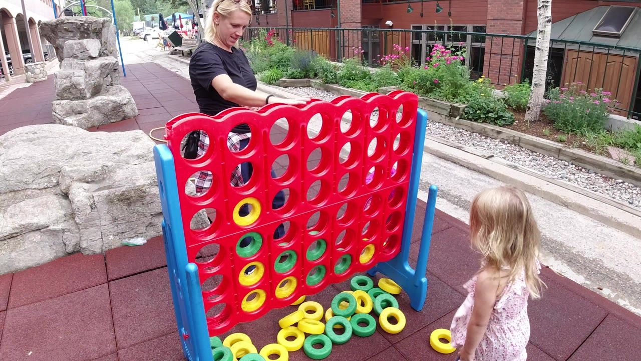 The child looks toward the giant red game board in Winter Park, Colorado, as the adult woman stands behind it with rings clustered along the bottom edge.