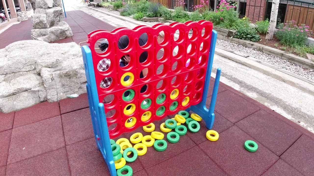 Large red and blue ring game stands on red rubber flooring in Winter Park, Colorado, with yellow and green rings in the board and no visible people.