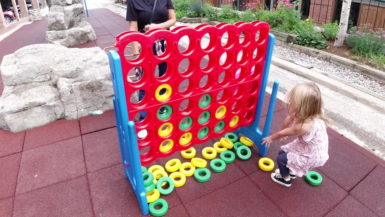 Young girl beside a giant red grid game with yellow and green rings.