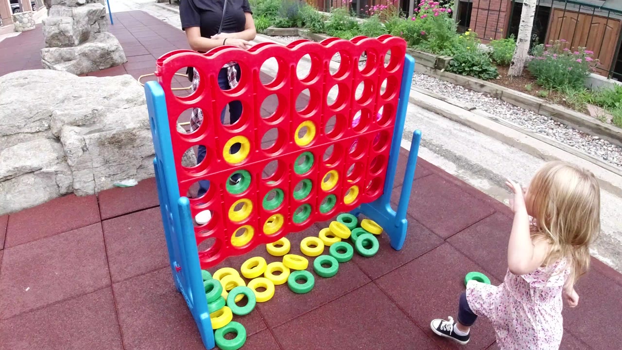 Child beside a giant red connect-four style game outdoors.