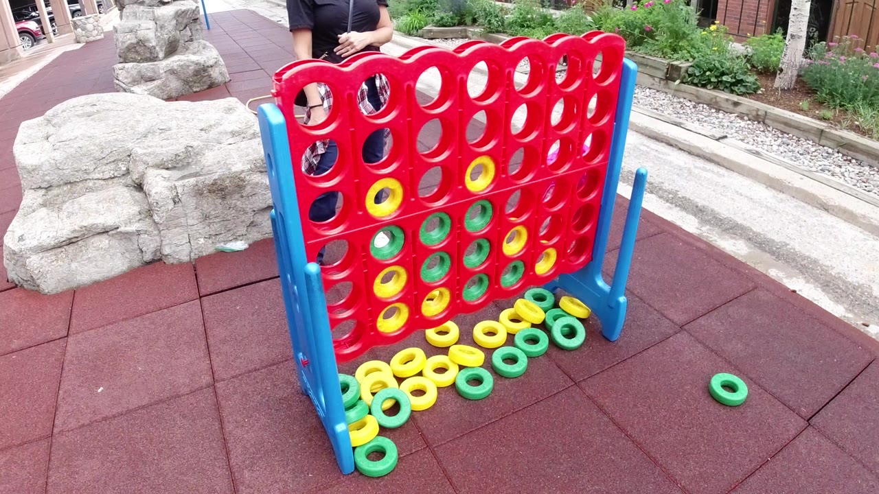 Oversized red game board with green and yellow rings on red outdoor flooring.